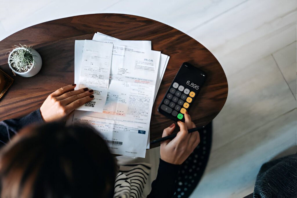 Overhead view of young Asian woman managing personal banking and finance at home. Planning budget and calculating expenses while checking her bills with calculator. Managing taxes and financial bills. Home budgeting. Concept of finance and economy illustrating business financial management system