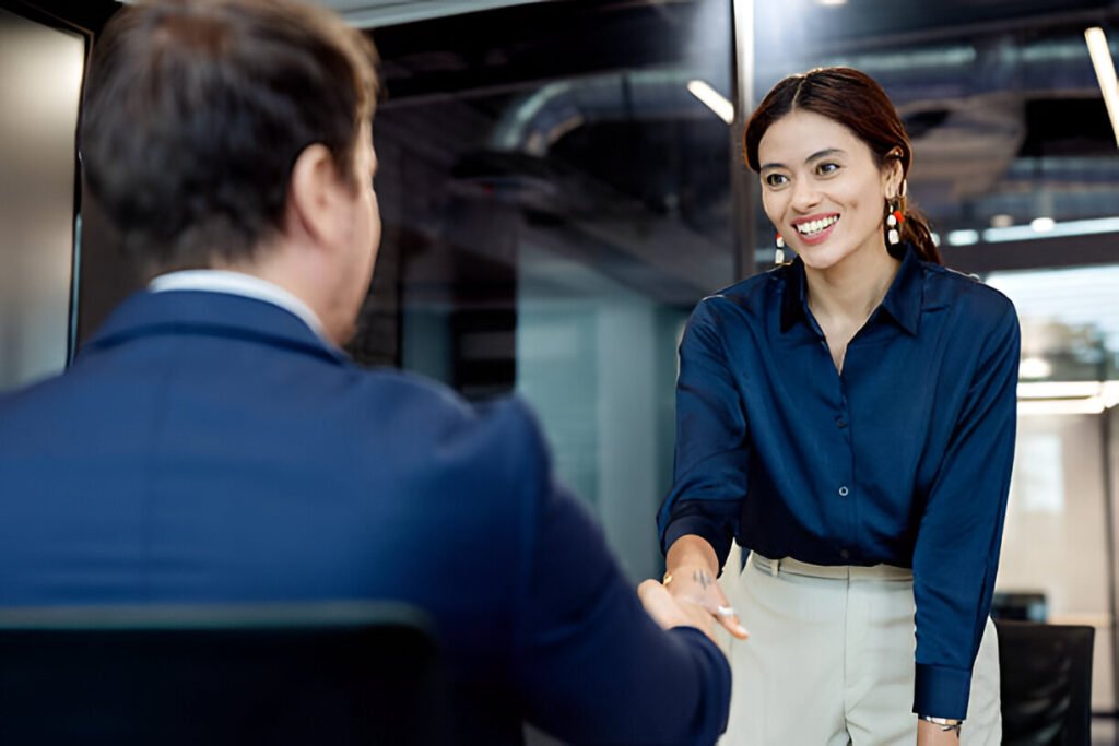 An Asian female candidate, newly selected as an employee, shakes hands with the recruitment manager in a modern business office conference room after completing her job interview, illustrating hiring process